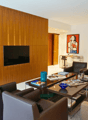Living room with modern interior, wooden wall, couch, chair, coffee table, tv, artwork, kitchen and dining area visible in background