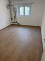 empty room, wooden floor, white walls, window with metal grill, pipes on the wall