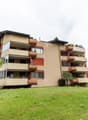 Apartment building with several floors, balconies, large front lawn, and potted plants on the balconies