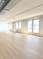 large room, hardwood floors, white walls, multiple windows, door at left, radiators