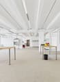 Empty office room with desks and fluorescent ceiling lights, carpeted floor