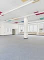 Empty room with gray carpeted floor, white walls, two sets of double doors, large windows, central pillar