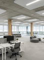 modern office space with desks, monitors, chairs, round sofa, windows, potted plants, and a central meeting area