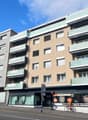 Apartment building with multiple stories and balconies, modern design with glass railings, located on a street with parked bicycle.