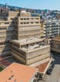 High rise office building with multiple floors, surrounded by urban landscape, several other buildings, green roofs, roads and vehicles