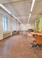 empty office with wooden floor, white walls, radiators, large windows, round and rectangular tables, chairs