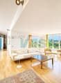 una stanza con un'ampia finestra, un pavimento in legno, un divano bianco e un tavolo in legno / a room with a large window, a wooden floor, a white couch, and a wooden table