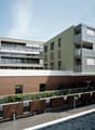 Multi-story apartment building with a modern, minimalist design. The building features a mix of materials including wood, glass, and brick. There are balconies on some of the units, providing outdoor space for the residents. The building appears to be par