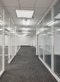 An empty, modern office space with glass walls and doors, and a gray carpet.