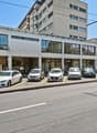 White commercial building with glass facades and several vehicles parked in front