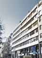 Multi-story building, white exterior, multiple windows, commercial space on the ground floor, trees in the vicinity