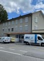 3 story building, grey exterior, multiple windows, awning, 2 vans parked in front
