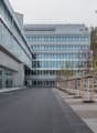 Multi-story office building with glass facade, surrounded by a paved outdoor area with benches and trees