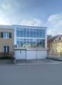 3 story house with a glass facade, garage doors, and an air conditioning unit in the middle, paved parking area in front