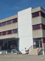 3-story commercial building, modern architectural design, multiple windows, stairs leading to the entrance, parking lot in front, adjacent building in the background