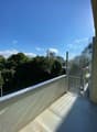 Outdoor balcony with railing and glass doors, clear view of trees and city buildings in the distance.