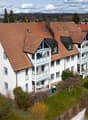 3-story house, brown roof, white walls, blue trim, multiple balconies, multiple windows, garden, solar panels