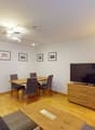 Living room with wooden floor, large windows, dining table, couch, TV, lamp, and modern interior