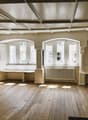 bare room with hardwood floors, white walls, arched windows, benches, radiator