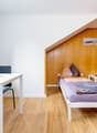 small room with a bed, desk, and chairs, wooden wall, window