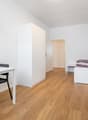 small room with a desk, two chairs, a bed, a wardrobe, a shelf, a television, and a washing machine