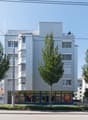A multi-story commercial building with a modern, minimalist design. The building has large windows, balconies, and is surrounded by trees. There are several retail stores on the ground floor, including a Sun store.
