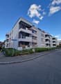 4-story modern apartment building with gray exterior, balconies, and landscaped grounds