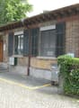 Brick building, black shutters, small garden, brown wooden door, paved walkway