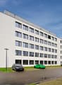 White modern office building, large windows, street lights, parking lot with multiple cars parked