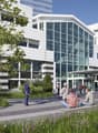 modern office building, glass facade, multiple floors, entrance with canopy, people walking, greenery, bicycle rider