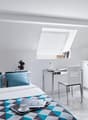 Single bedroom with bed, desk, chair, small kitchenette, bedspread, decorative items, window with skylight
