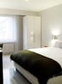 modern bedroom with a king size bed, white walls, large window, white cabinet, desk, white linens, plants