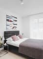 Modern design with white walls, black furniture, double bed, bedside tables with lamps, TV, painting, nightstand with candle and flower vase