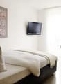 single bed, modern design, mounted TV, decorative painting, white pillow, black cushioned chair