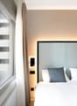 Double bed, large window with view of mountains, white walls, two bedside lights, gray headboard, white sheets, gray pillows