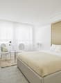 Modern styled bedroom with a bed, nightstands, two chairs, round coffee table, plant, and a TV mounted on the wall. Includes a desk, chairs, and a rug.