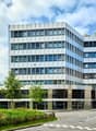 Modern office building, multiple floors, glass windows, metallic façade, greenery around