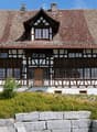 2 story house, brown roof, white and brown wooden facade, wooden balcony, chimneys, large windows