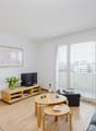 Bright and spacious living room with hardwood floors, white walls, large windows, TV stand, coffee table, and sofa