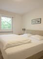 Spacious bedroom with large windows overlooking greenery, white walls, hardwood floors, a king-size bed with white bedding, a wooden nightstand, and a framed artwork on the wall.