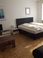 a bedroom with wooden floor, large bed, night table, TV on TV stand, a table, and a couch