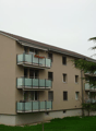 3 story apartment building, beige exterior, multiple balconies, green lawn, trees