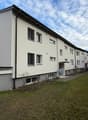 Modern apartment building, white exterior, multiple windows, green lawn in front, pathway leading to entrance