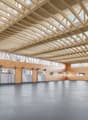 Large open space, metal gray doors, wooden trusses on ceiling, glass windows, brown walls, concrete floor