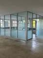 The image shows a large, open office space with concrete floors and glass partition walls. The space appears to be in a state of renovation or construction, with some debris on the floor. The glass partitions divide the space into separate rooms or areas,