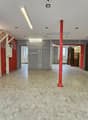 empty room, gray floor, red walls, red pillar, fluorescent ceiling lights, two doors, metal racks on the wall