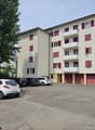 4-story apartment building with beige exterior and red shutters, parking lot in front with several cars parked