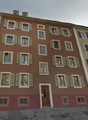 3 story building, brown walls, green shutters, wooden door, windows