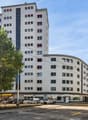 modern multistory residential building, glass windows, storefront on the ground floor, parking lot in front