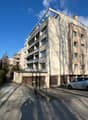 5-story building, beige exterior, multiple balconies, garage entrance, shadow of person and trees